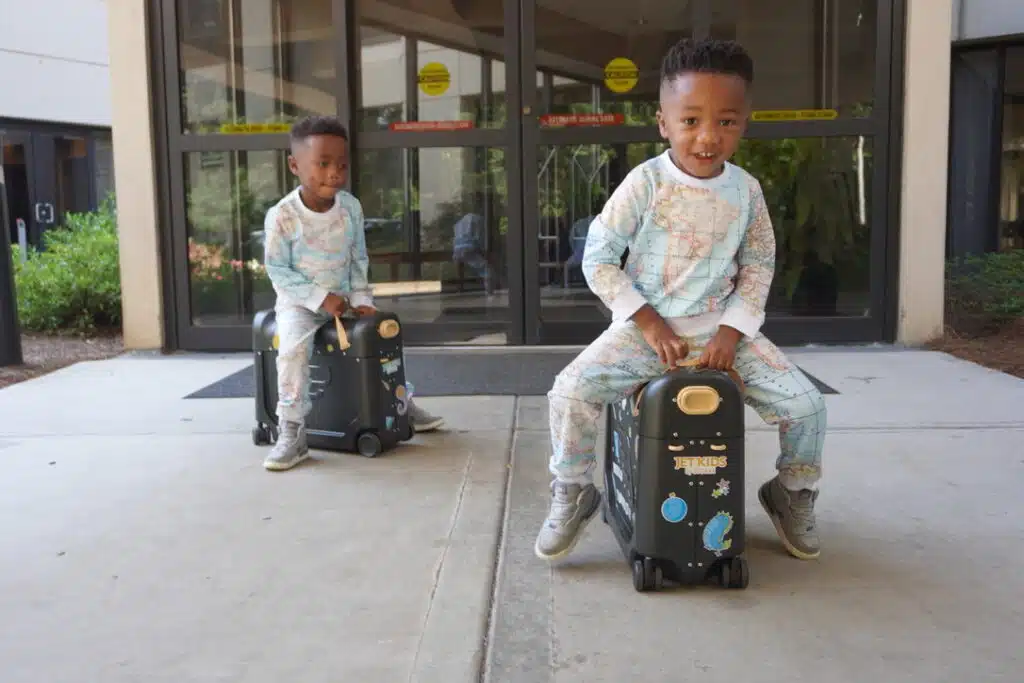 Twin toddlers using their JetKids Bed Box toddler airplane beds to race through the airport.