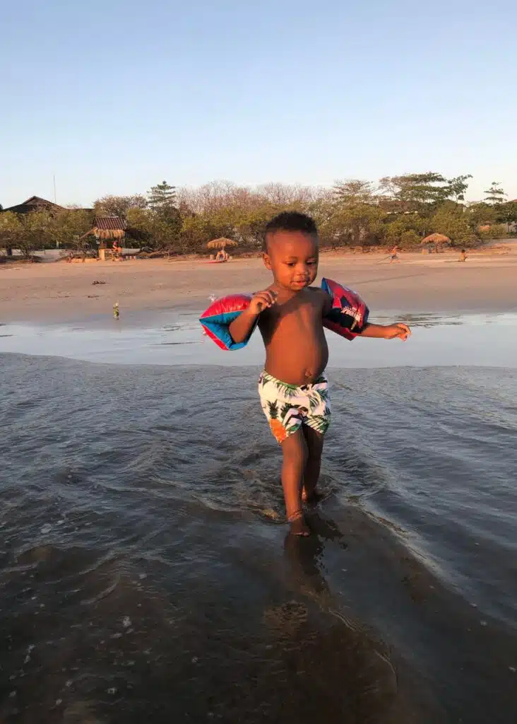 A toddler testing the beach water in Tamarindo with his floaties on his arms.