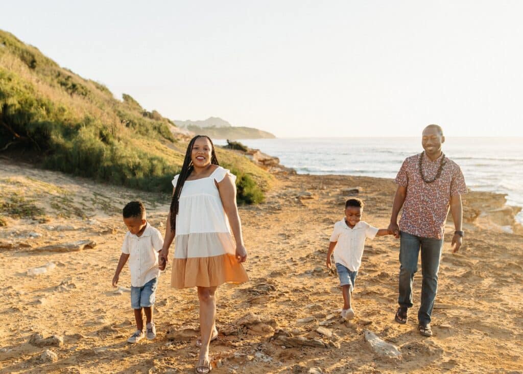 My family taking a cute photo at sunset walking down the beach. The boys wearing matching white shirts and shorts and a white/orange sundress for myself. Cute sundresses are the best answer to the question: what to wear in Hawaii?