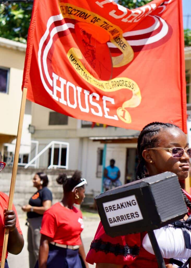High school students carrying flags and signs that say "breaking barriers" on the streets of Grenada.