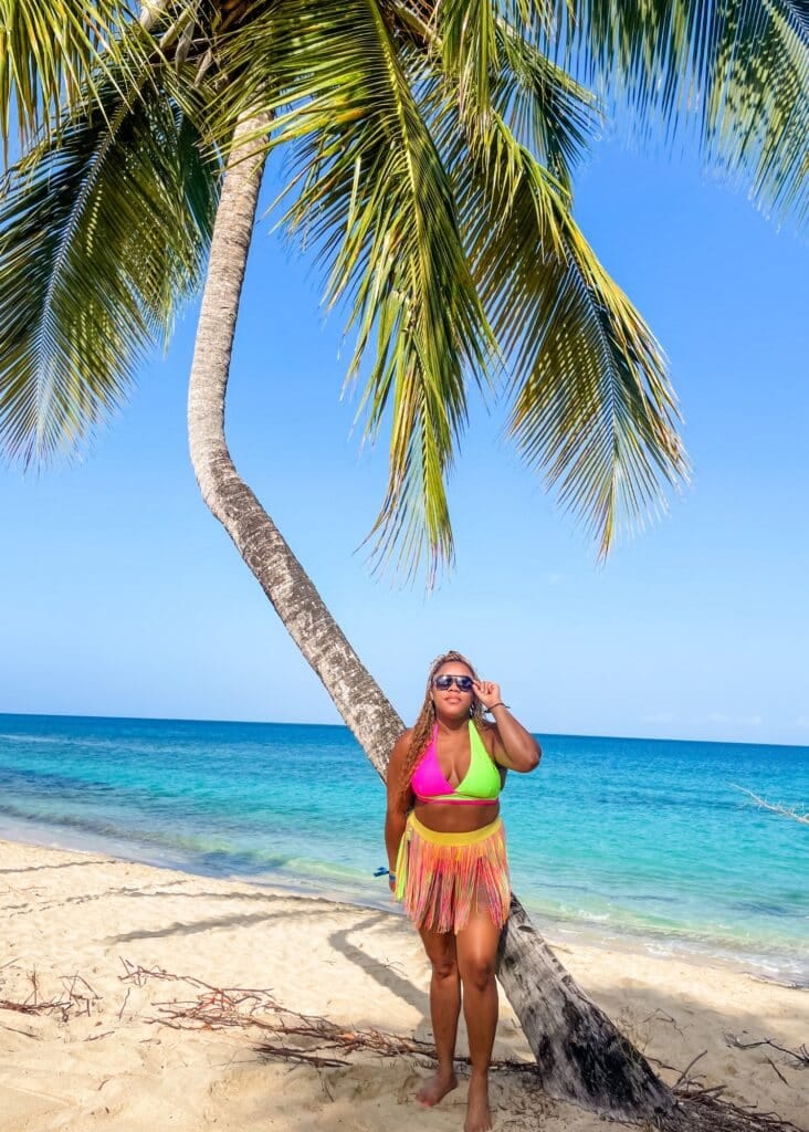 Me standing on the beach in Grenada wearing a colorful swimsuit and sunglasses. Visiting Grenada is perfect for beach lovers!