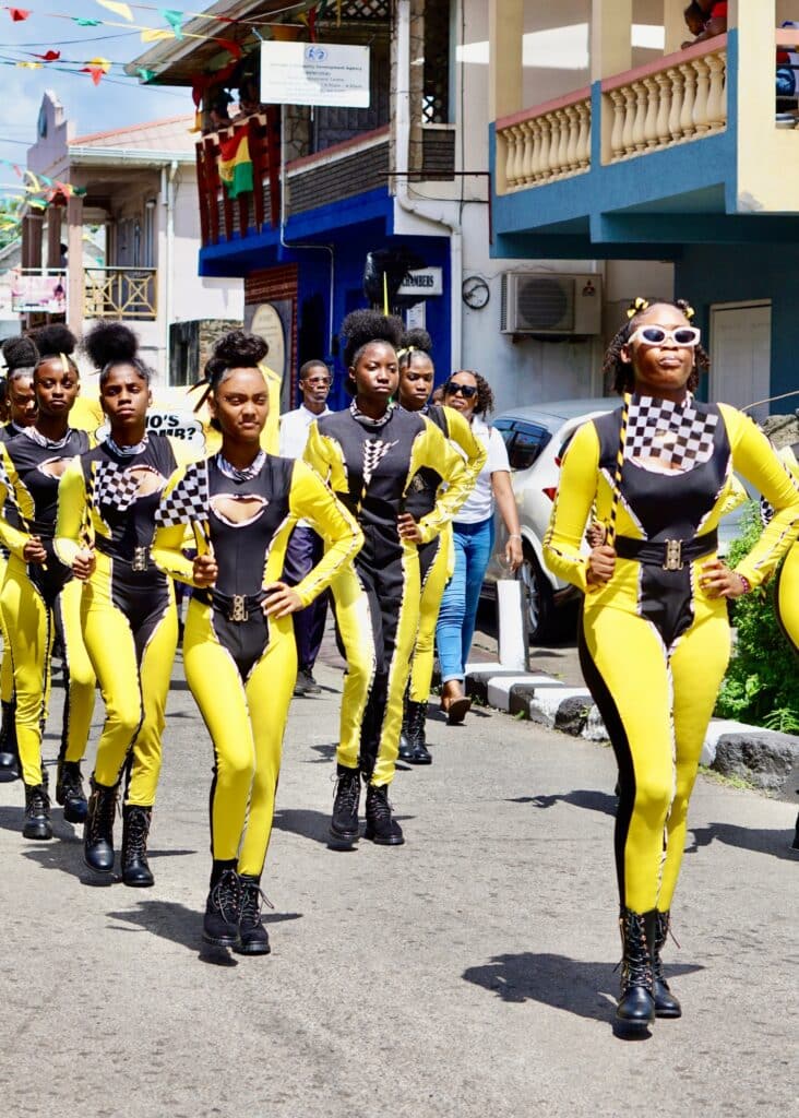 High school students marching in matching bright yellow and black jumpsuits in a parade on the streets of Grenada.