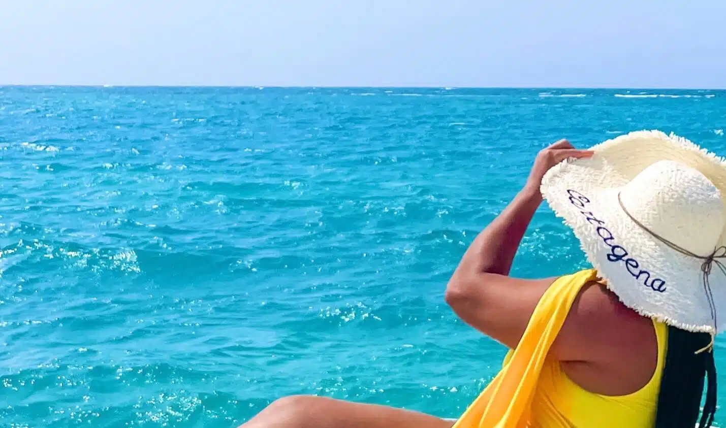 Sitting on a boat in Rosario Islands wearing a yellow swimsuit and a hat that says "Cartagena"