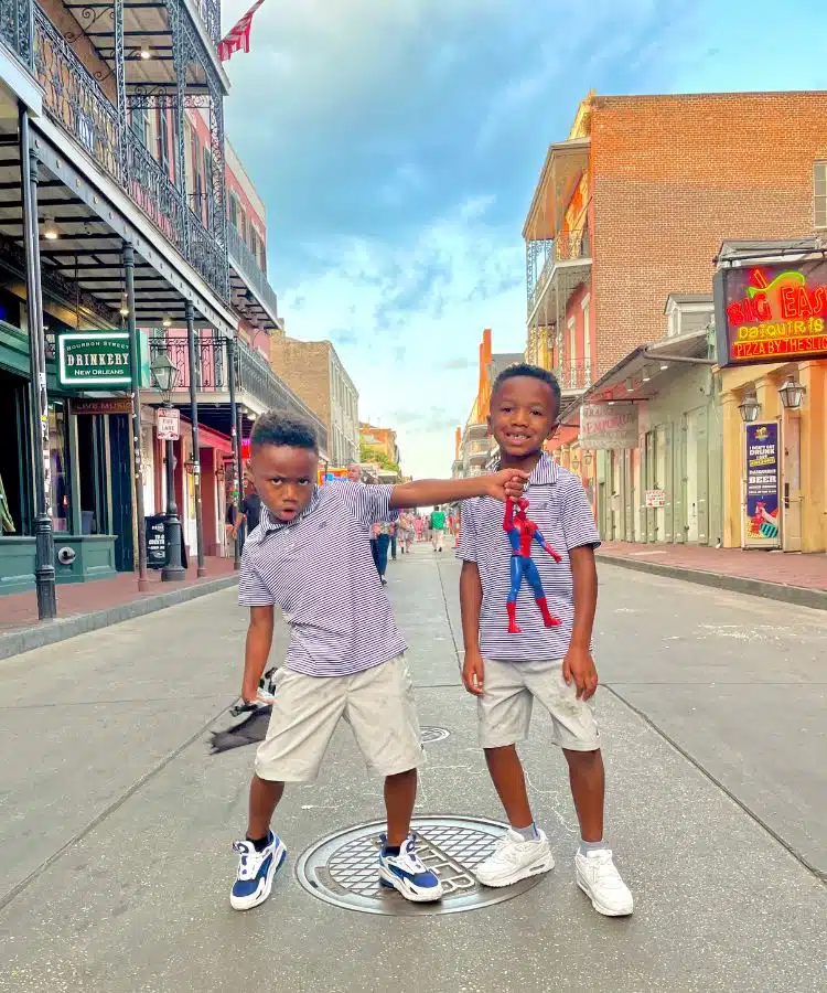 Twin boys posing on Bourbon Street with Batman and Superman in hand