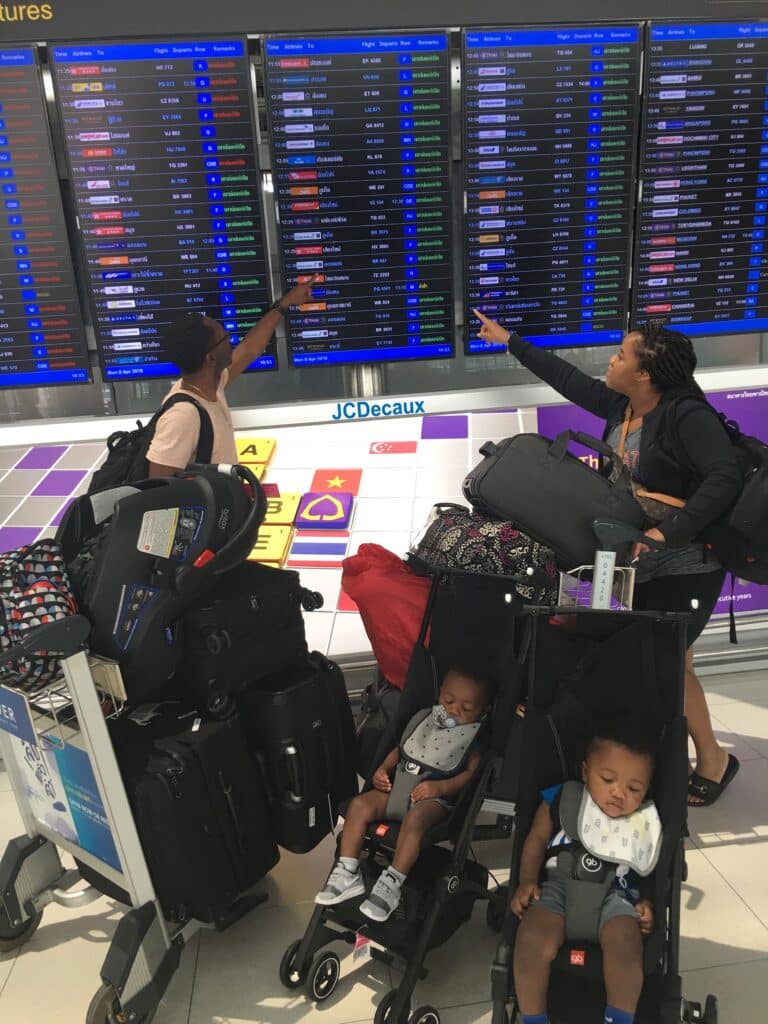 my husband, twin toddlers, and I at the airport with all of our luggage looking at the arrival/departure screen