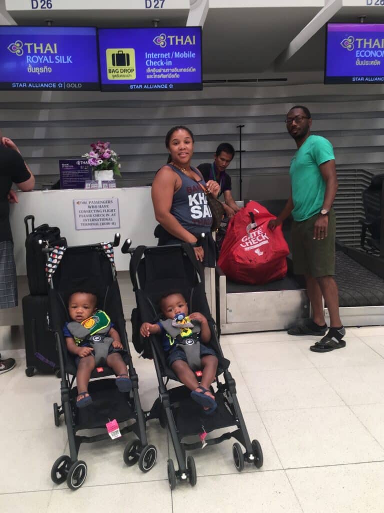 My twin boys sitting in their GB Pockit Strollers at the airport check-in counter, while my husband and I check in car seats