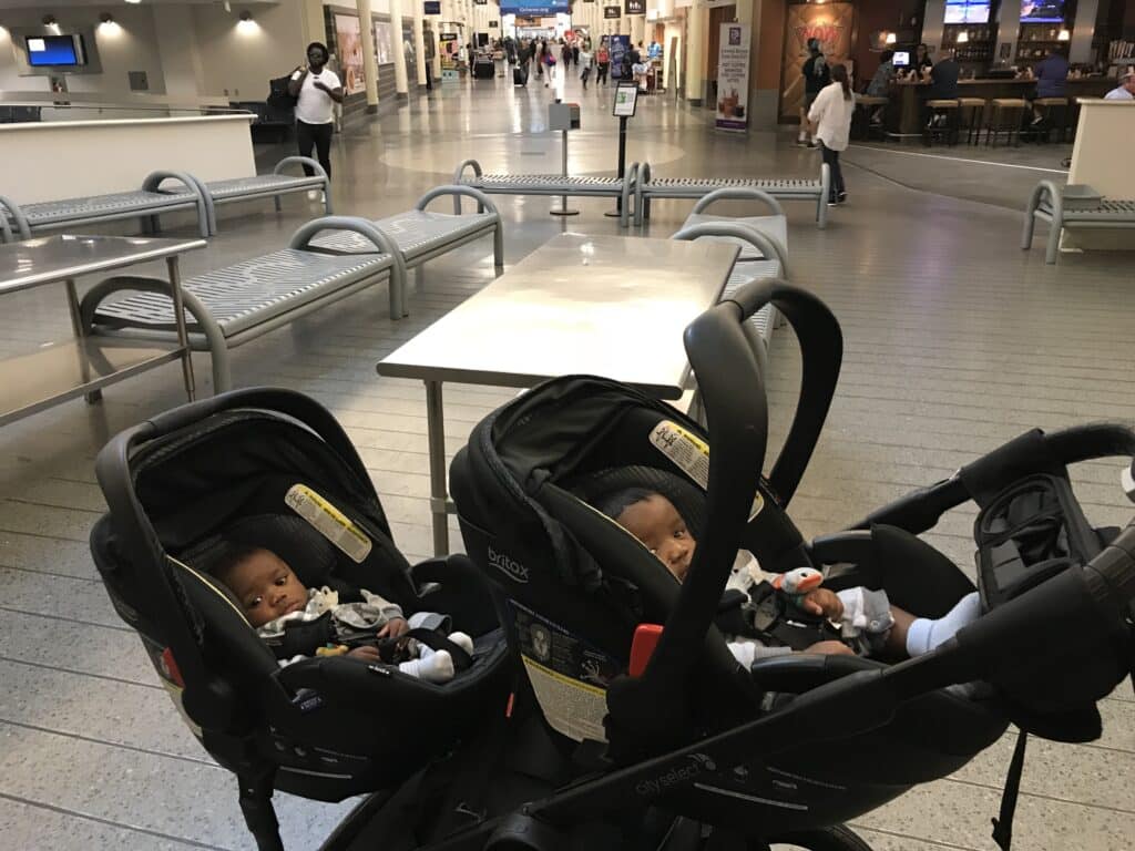 Twin babies sitting in their double strollers at the airport- for their first flight.