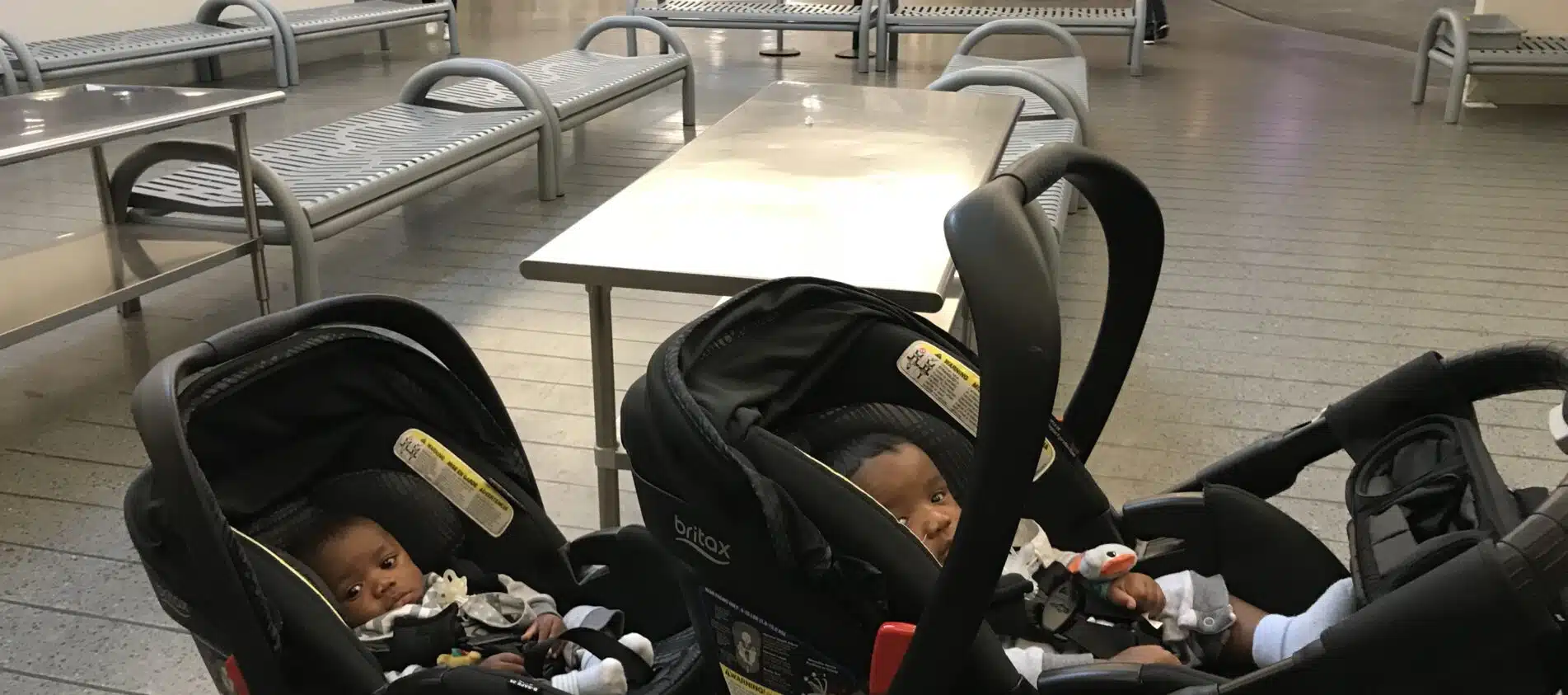 Twin babies sitting in their double strollers at the airport security- for their first flight.