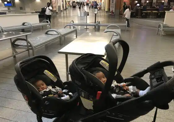 Twin babies sitting in their double strollers at the airport- for their first flight.