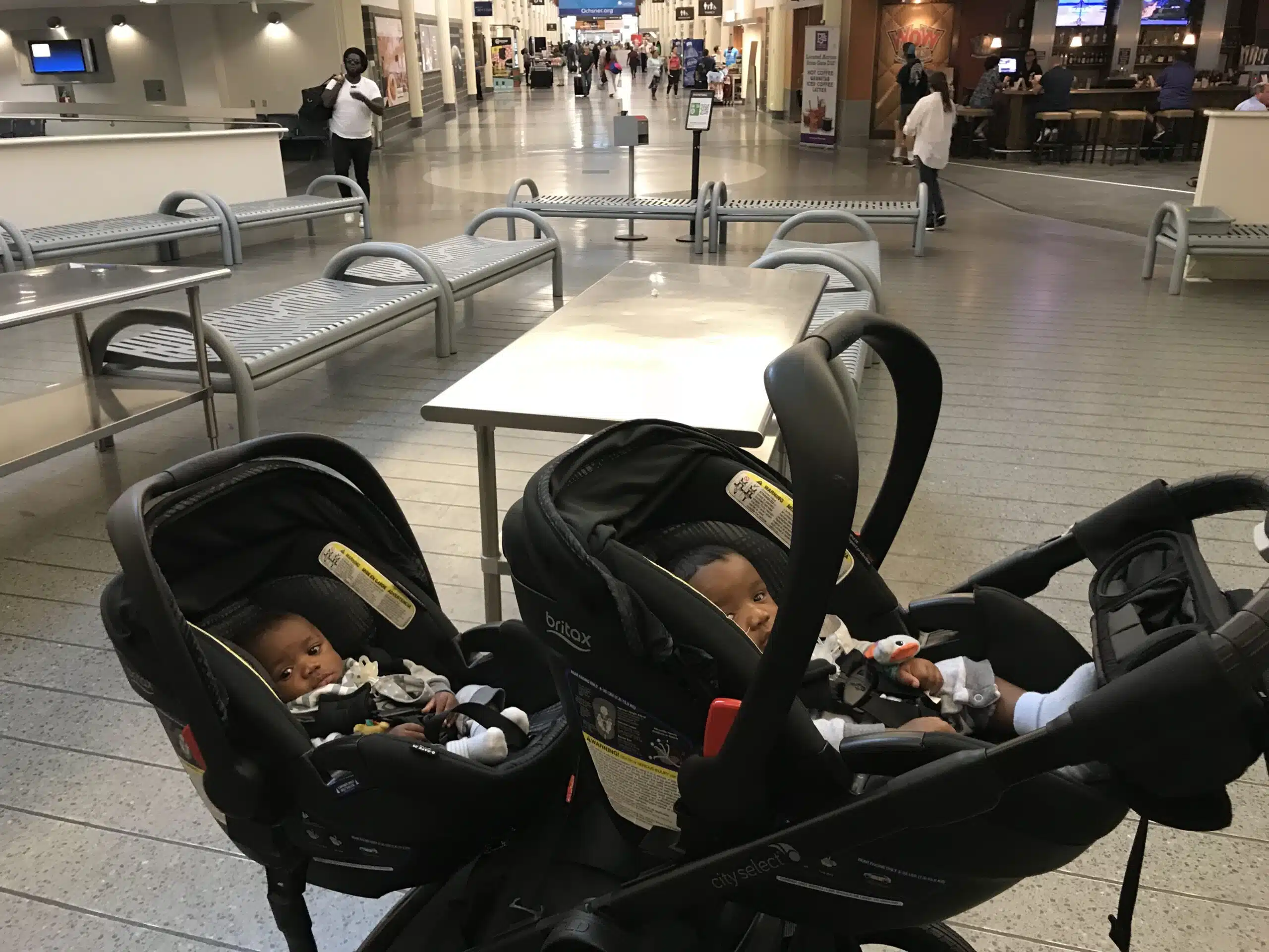 Twin babies sitting in their double strollers at the airport- for their first flight.