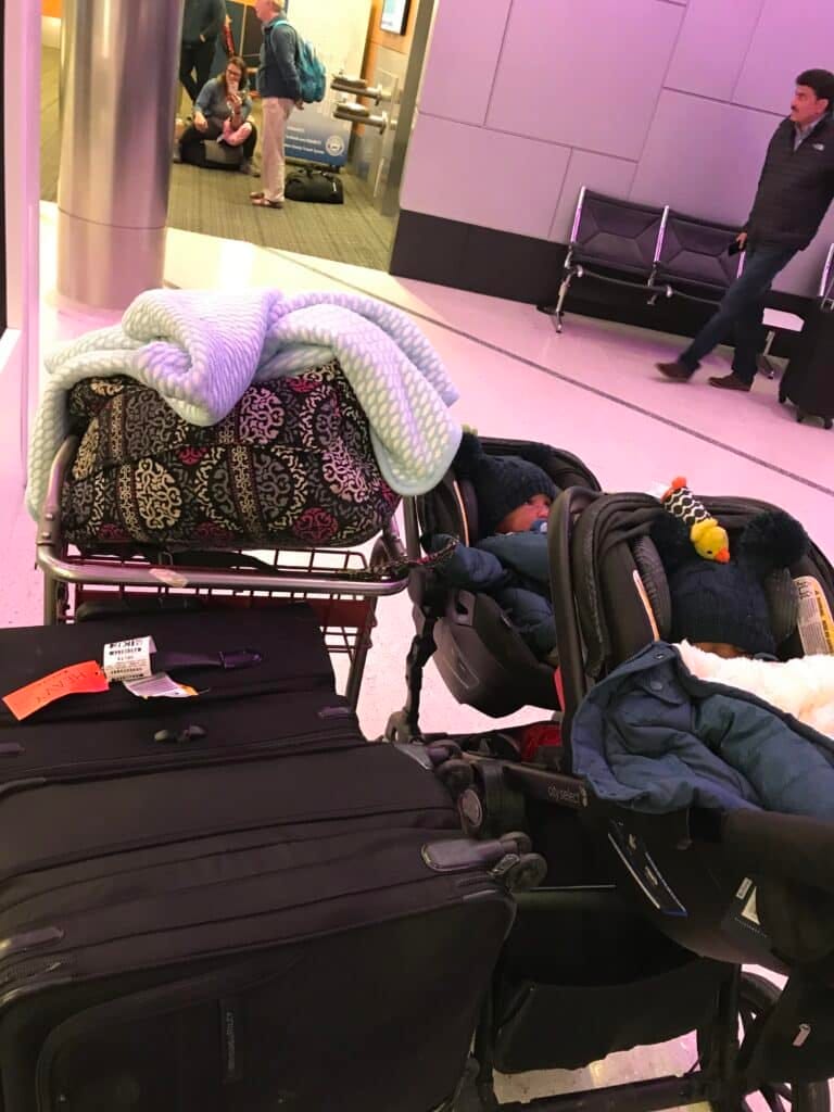 My twins sitting in their double stroller with car seats, surrounded around a ton of luggage
