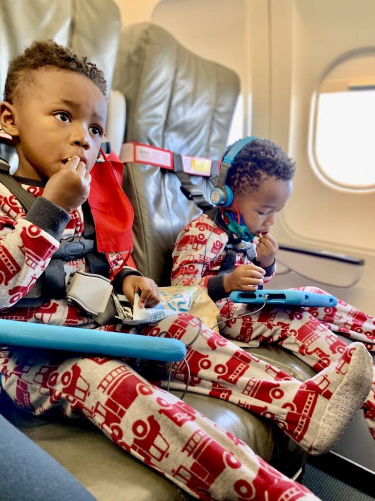 My twin boys sitting on the airplane using their CARES, 5-point harness, with their tablets in hand. 