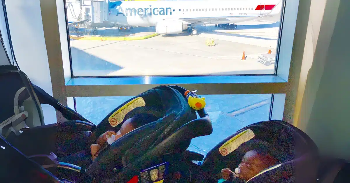 Twin babies sitting in their double stroller at the airport with an American Airlines plane in the background