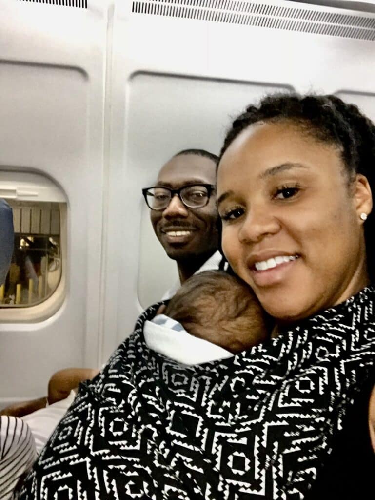 Parents sitting on an airplane with twin boys, one wrapped in a baby wearer.