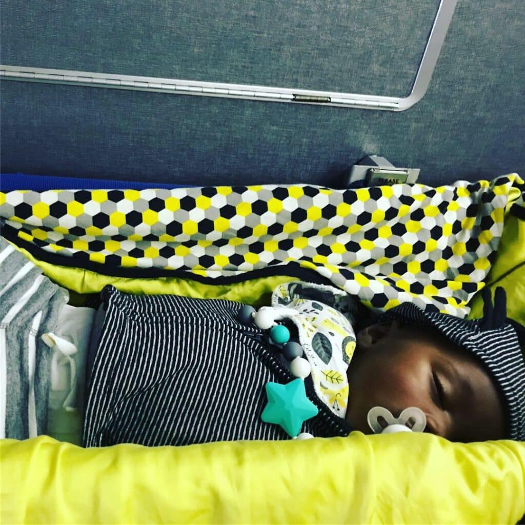 baby sleeping on an airplane bassinet connected to the bulkhead