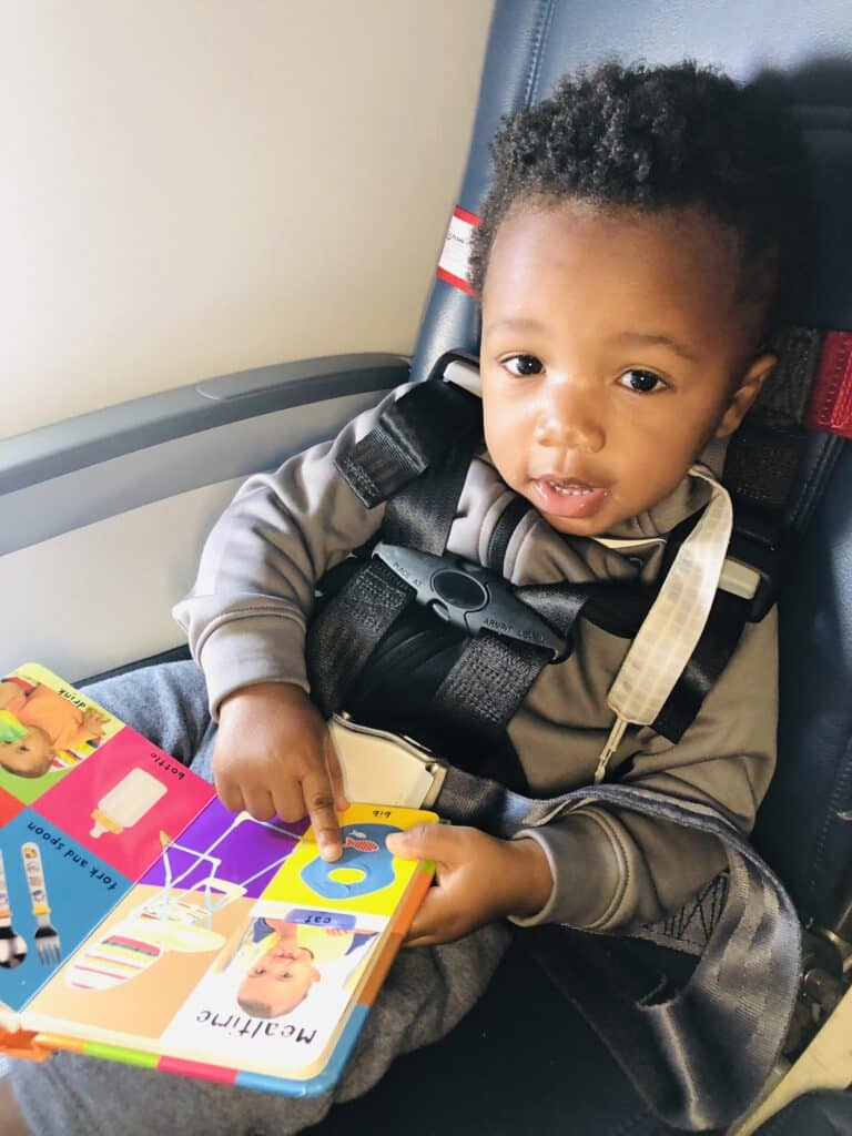 young toddler sitting on an airplane seat with a soft book in hand