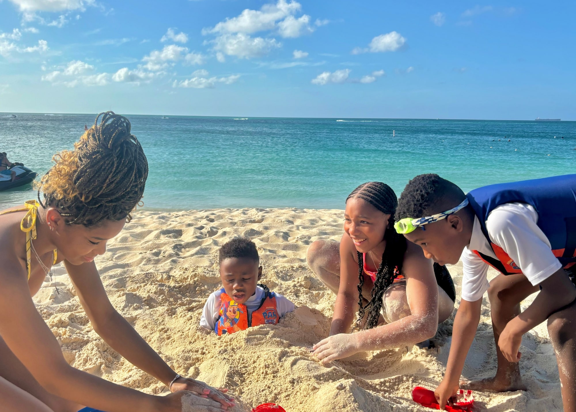 Marquita’s family plays in the sand on Eagle Beach in Aruba, with bright blue water and a clear sky in the background.
