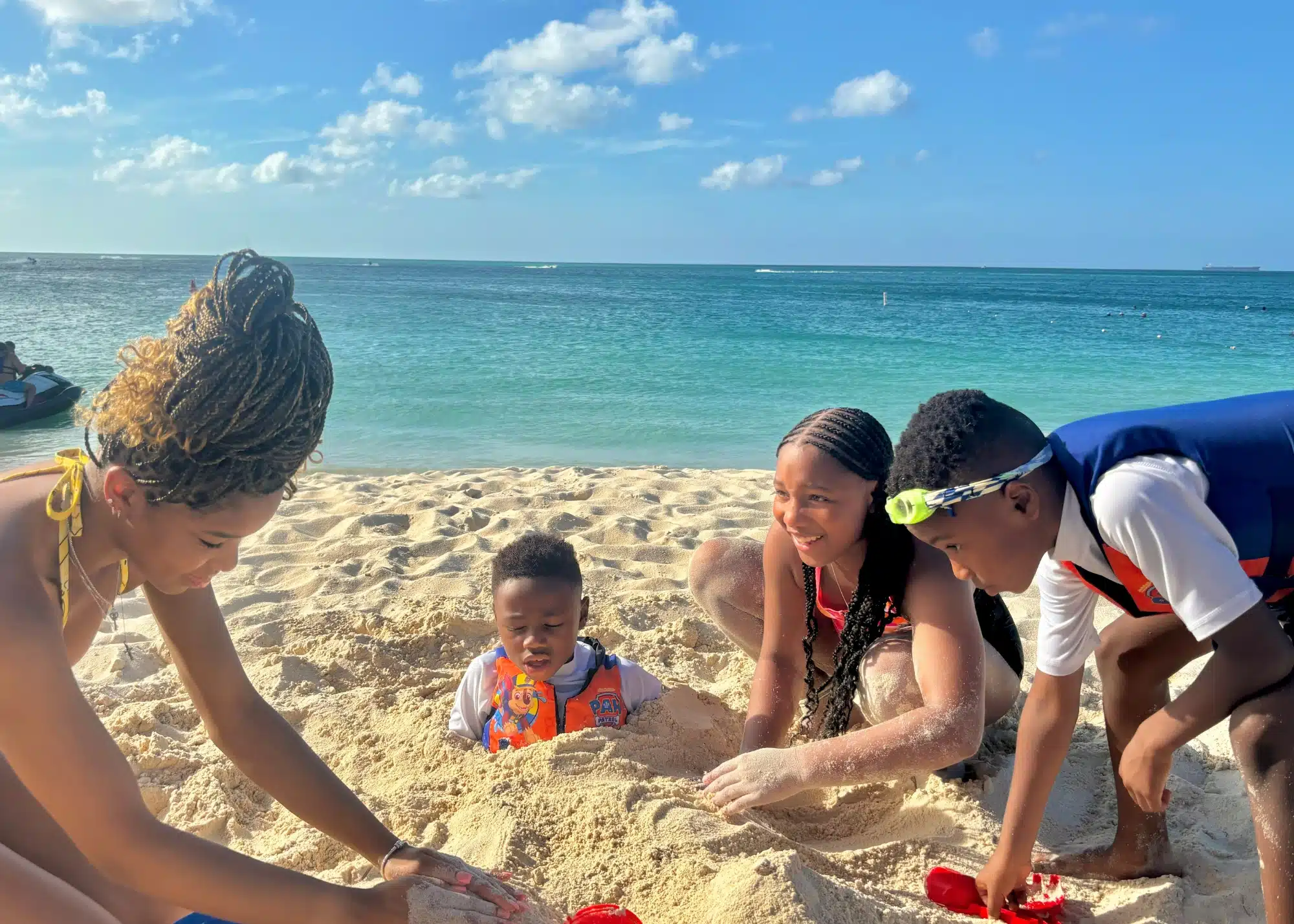 Marquita’s family plays in the sand on Eagle Beach in Aruba, with bright blue water and a clear sky in the background.