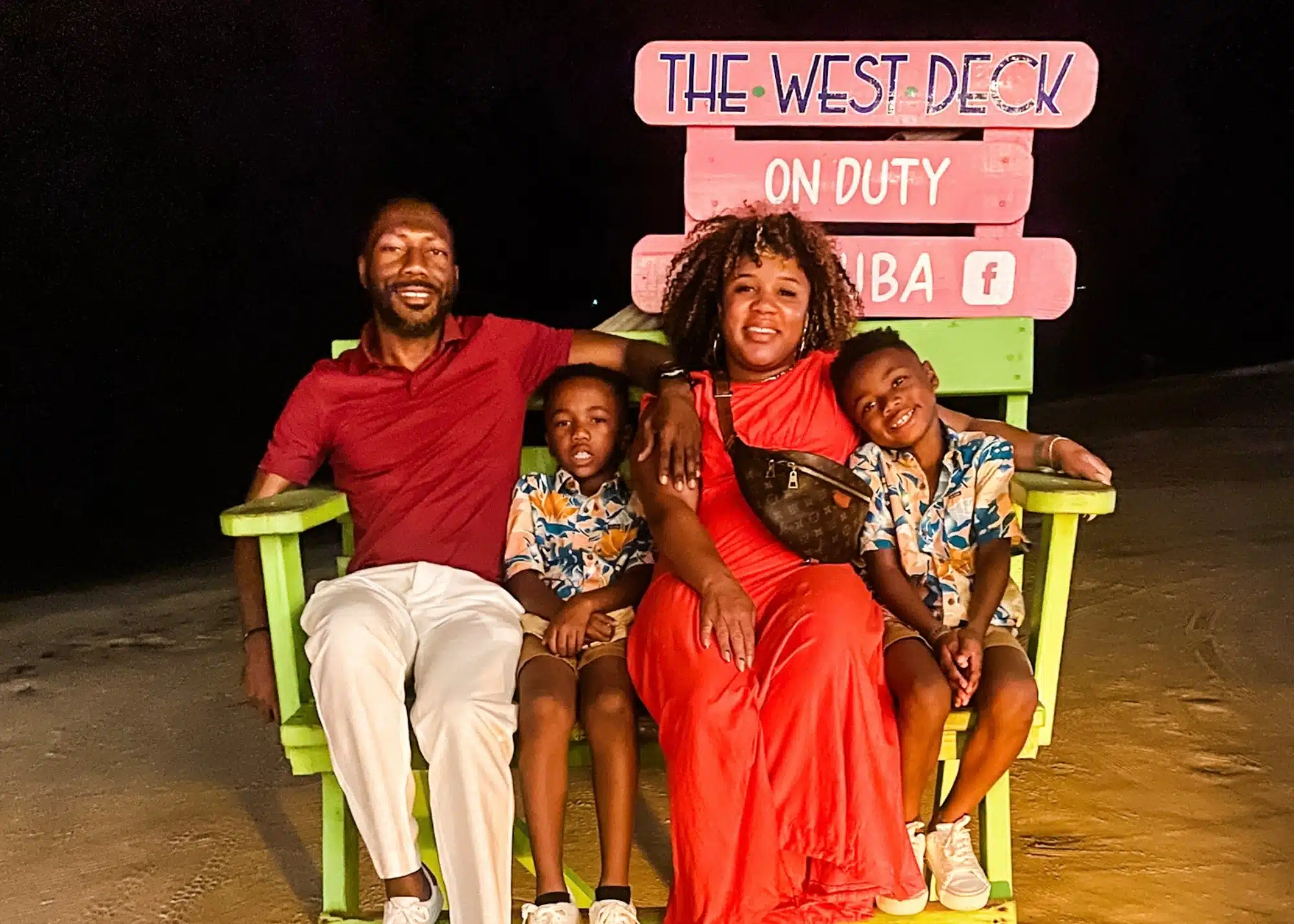 Marquita and her family sit together on a giant lime green beach chair at The West Deck in Aruba, smiling under the glow of evening lights.