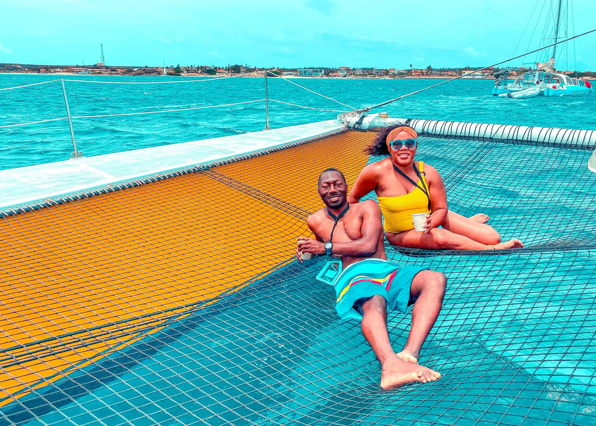 Marquita and her husband relaxing on the net of a catamaran with drinks in hand, surrounded by the deep blue waters of Aruba.