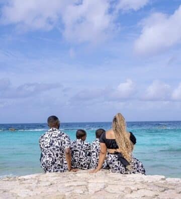 Mom and dad with twin boys sitting on a bed of rocks, facing the ocean.