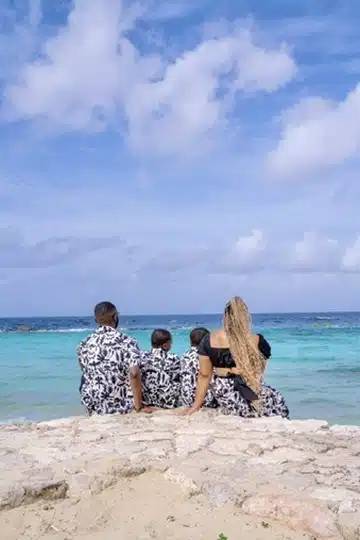 Mom and dad with twin boys sitting on a bed of rocks, facing the ocean.