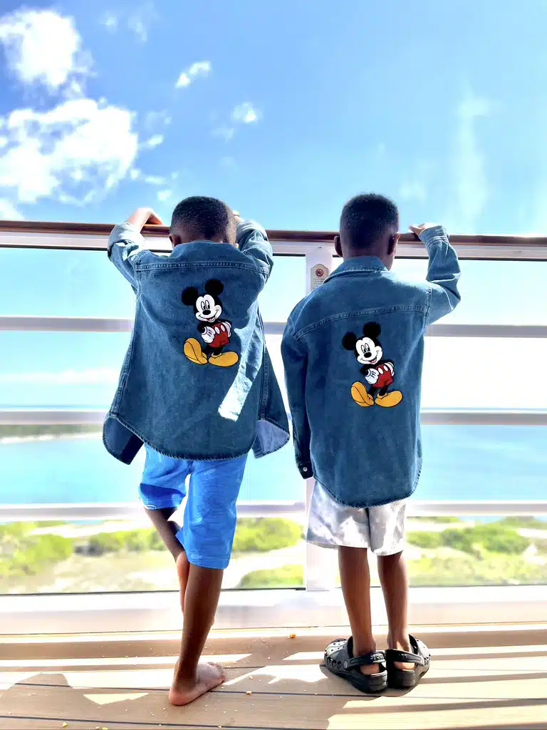Twin boys standing at the balcony on the Disney Wish, wearing a denim jacket with a big Mickey on the back.