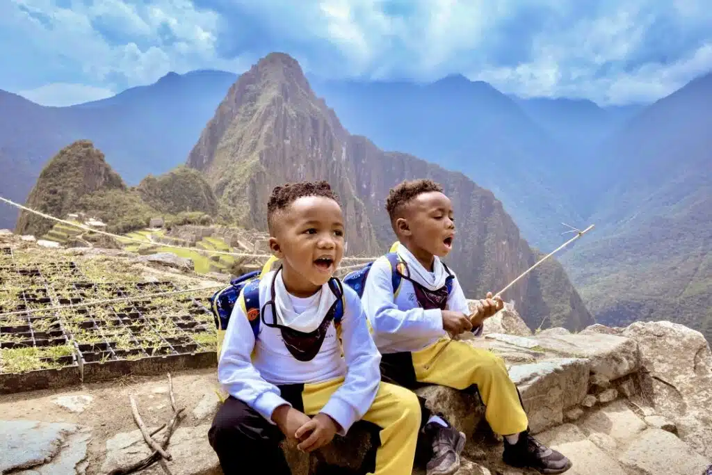 Twin boys sitting in front of the Machu Picchu village. One is holding a stick