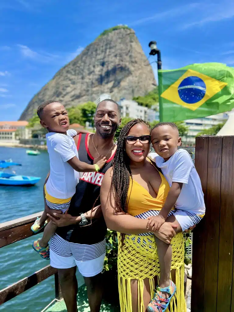 Mom and dad, holding twin toddlers, in front of the Brazil flag