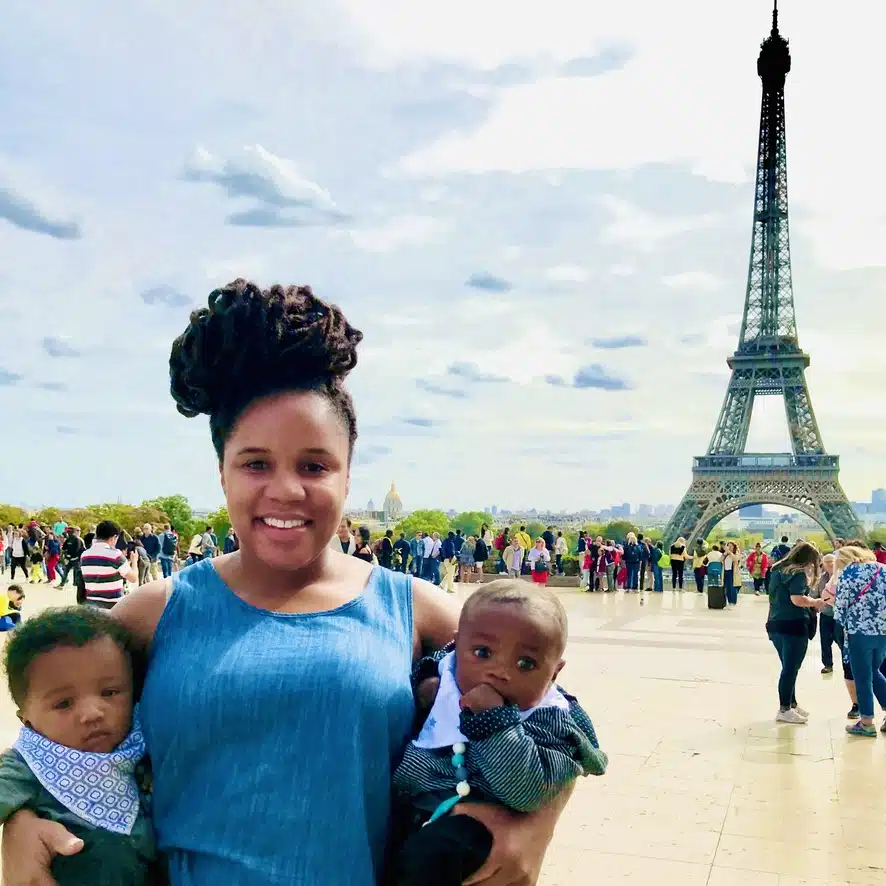 Mom holding twin 6 month old boys in front of the Eiffel Tower