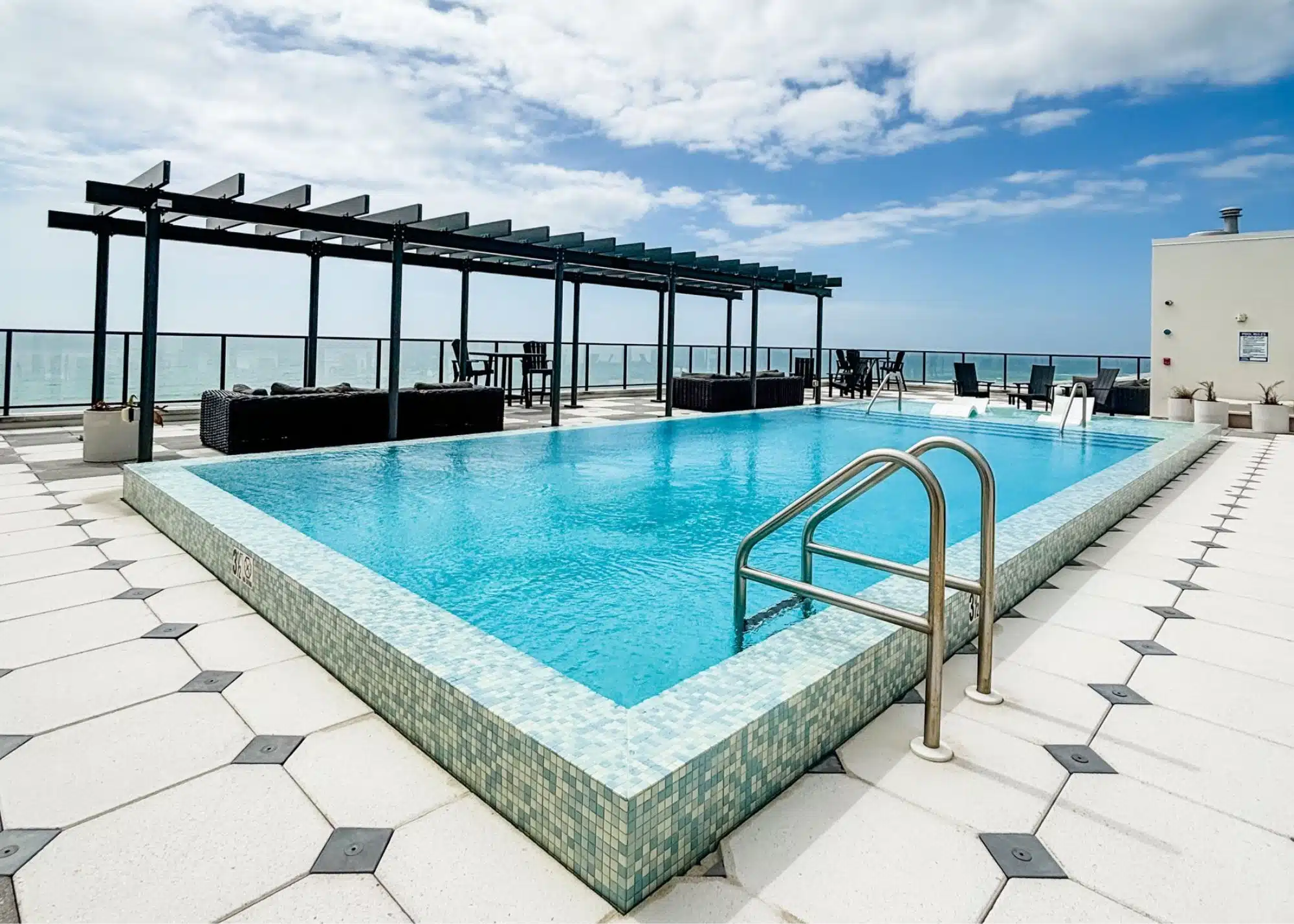 Rooftop swimming pool at the family’s beachfront vacation rental in Gulf Shores Alabama. Lounge areas surround the pool with views toward the Gulf beyond the glass railing.