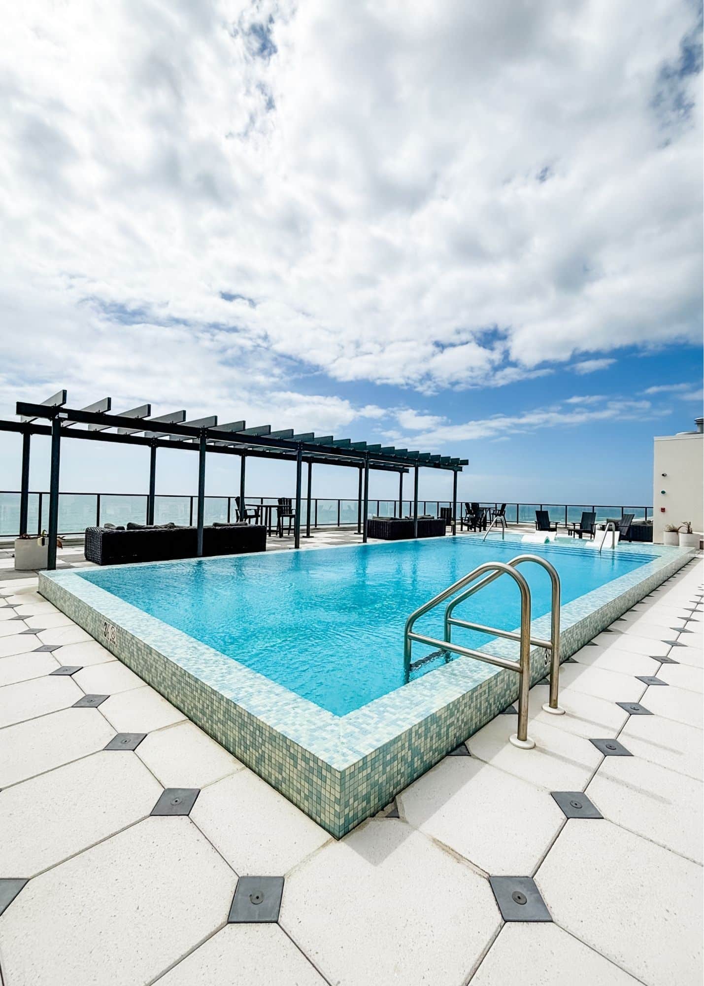 Rooftop swimming pool at the family’s beachfront vacation rental in Gulf Shores Alabama. Lounge areas surround the pool with views toward the Gulf beyond the glass railing.