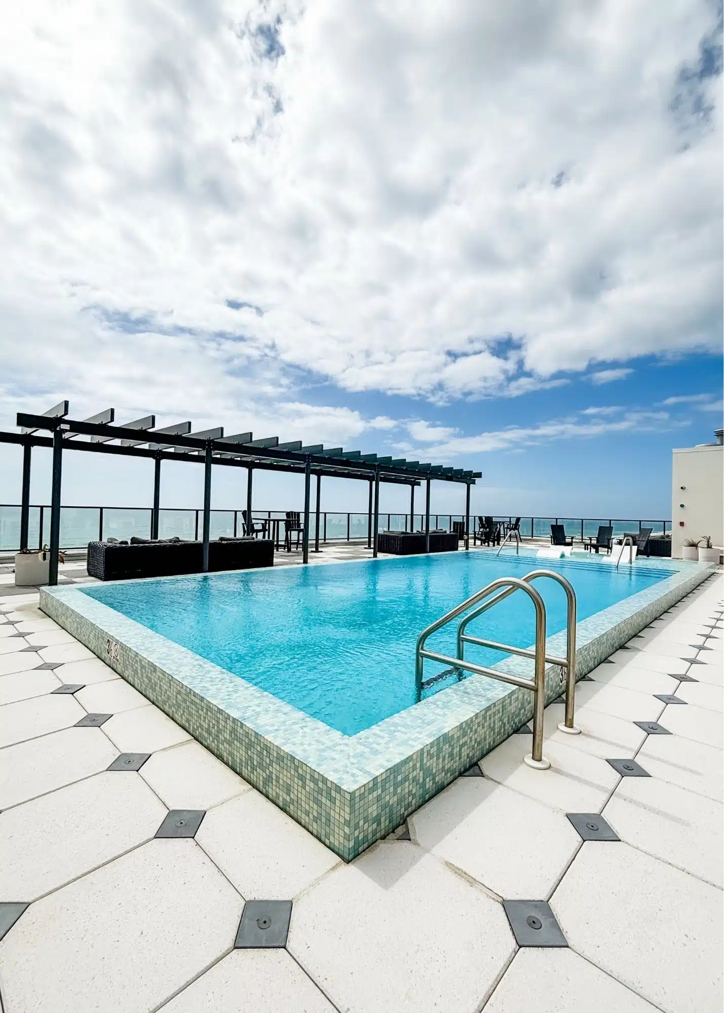 Rooftop swimming pool at the family’s beachfront vacation rental in Gulf Shores Alabama. Lounge areas surround the pool with views toward the Gulf beyond the glass railing.