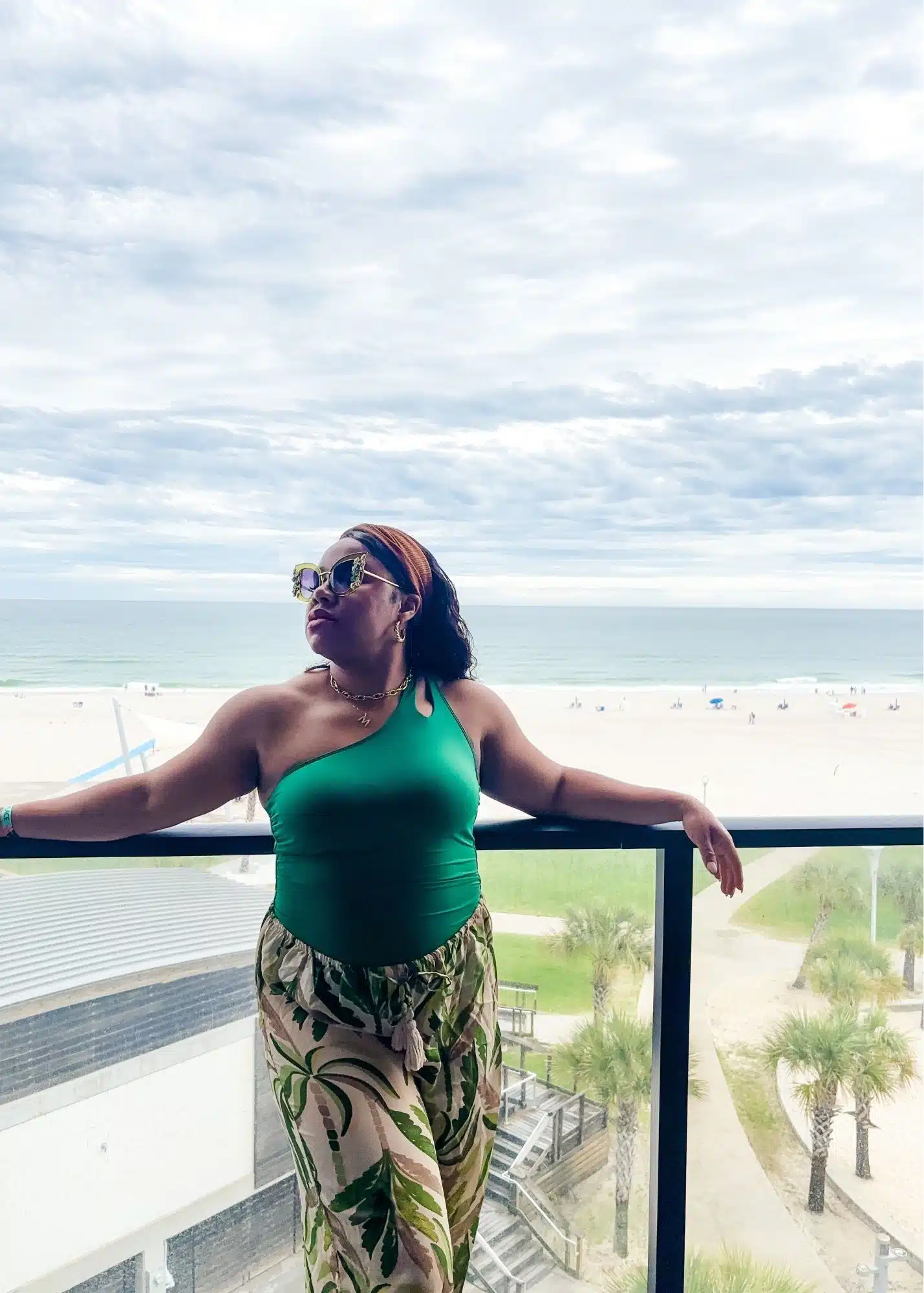 Marquita poses on a balcony overlooking the beach and Gulf of Mexico in Gulf Shores Alabama. Palm trees and white sand line the shoreline below her.