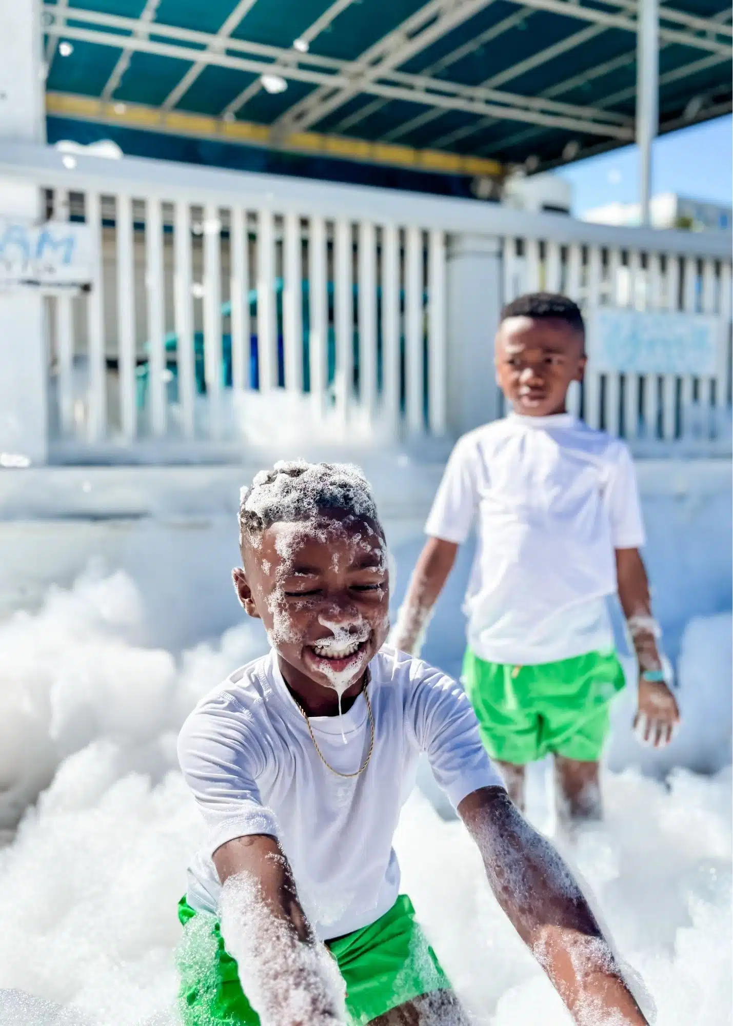 Marquita’s sons play together in piles of bubbles during the foam party at The Hangout. One boy laughs with foam covering his face and hair while his brother stands behind him.