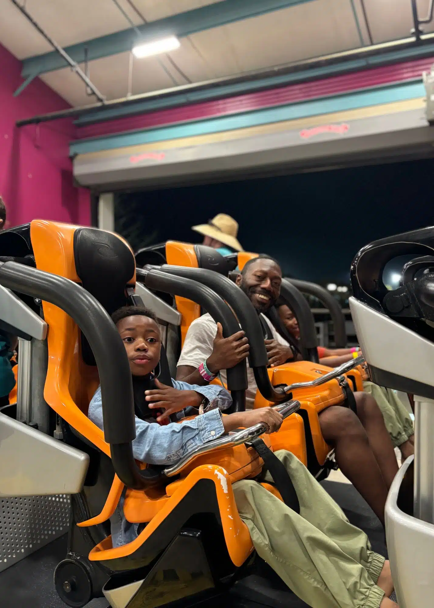 Marquita’s sons and husband sit together in orange seats with over the shoulder restraints before a ride at Tropic Falls.