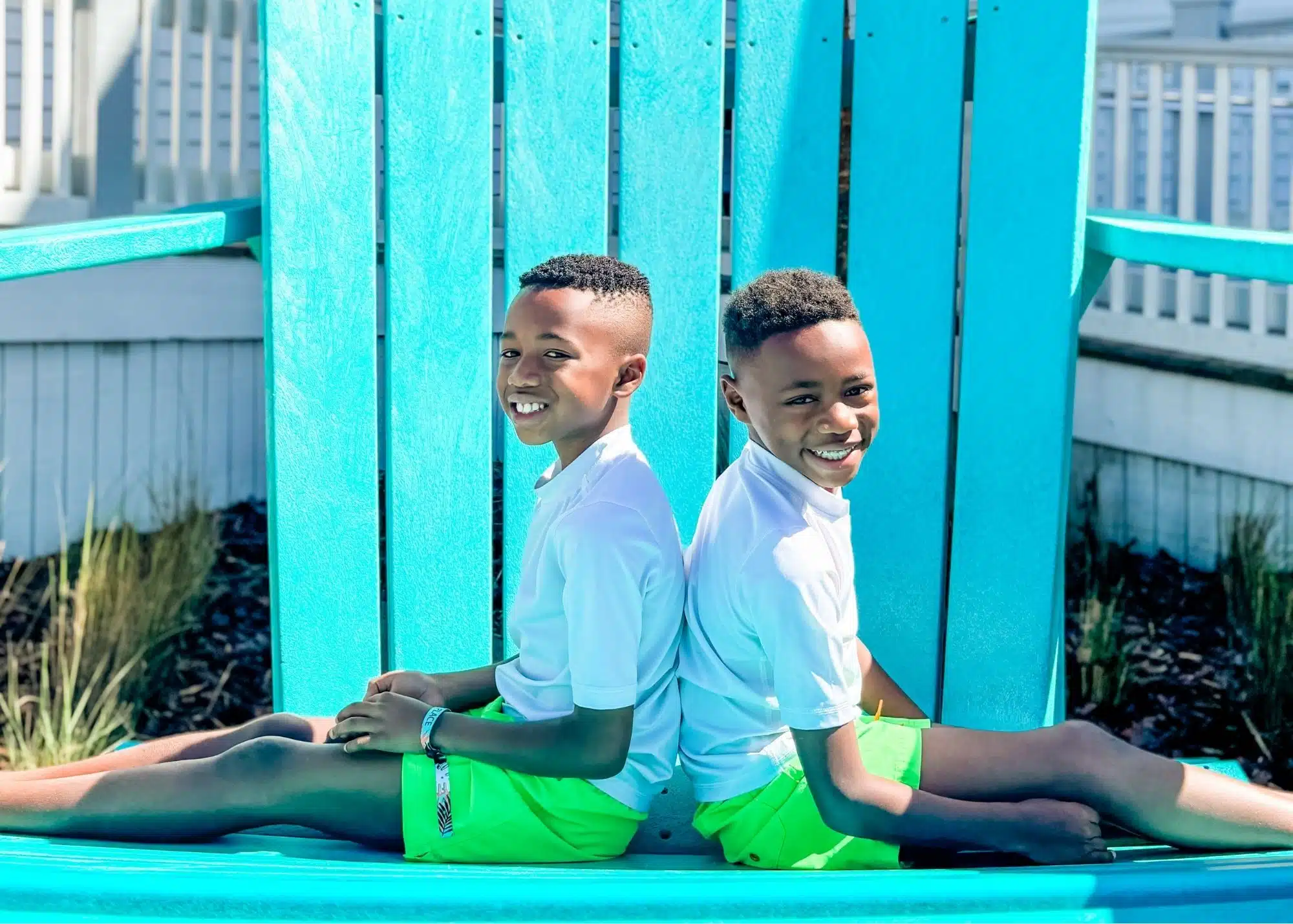 Marquita’s sons smile while posing back to back on an oversized turquoise chair at The Hangout in Gulf Shores. They wear matching white shirts and bright green shorts during their family trip to Alabama.