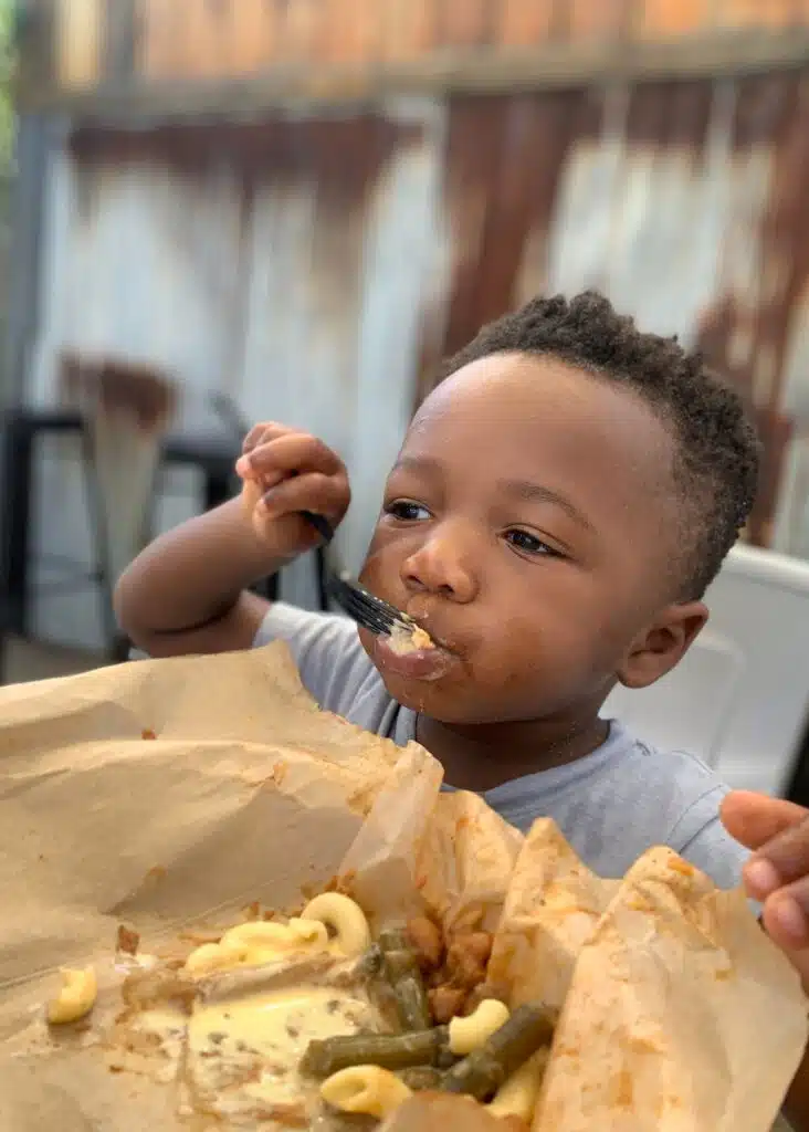 One of Marquita’s sons takes a bite during an outdoor meal at Hog Wild Beach and BBQ. His tray has macaroni and cheese and green beans covered in barbecue sauce.