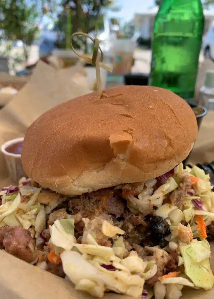 A piled high barbecue sandwich at Hog Wild Beach and BBQ is stuffed with smoked meat and crunchy coleslaw beneath a soft bun.